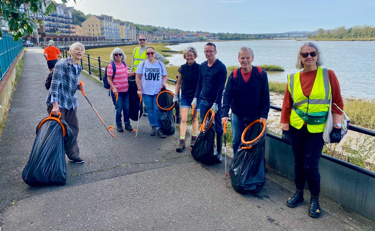 Volunteers pose with litter picking equipment on a walkway beside the River Medway