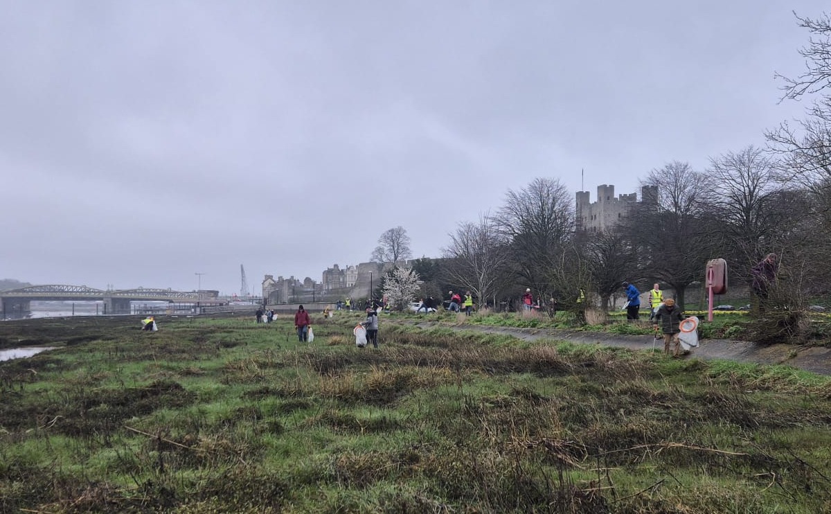 Volunteers collecting litter from the marshy foreshore of the River Medway with Rochester Bridge and Rochester Castle in the background