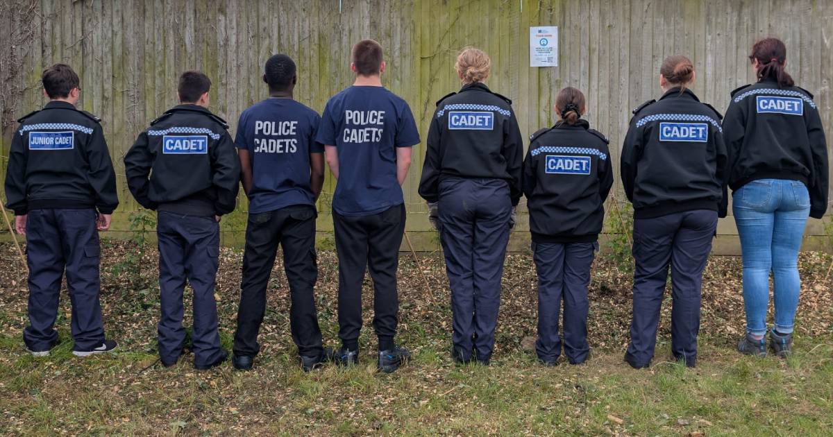 A row of police cadets, facing away from the camera to show the "Cadet" markings on their jackets