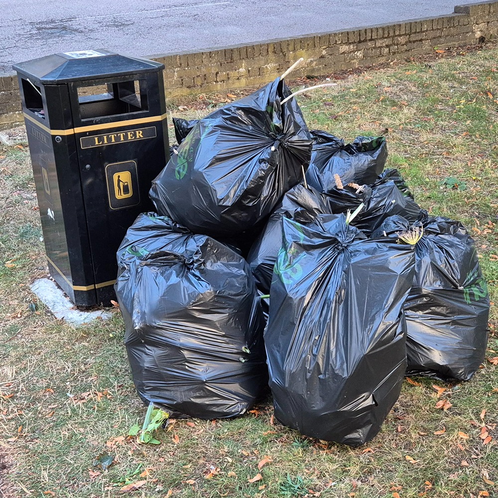Eight black refuse sacks filled with garden waste await collection by a litter bin