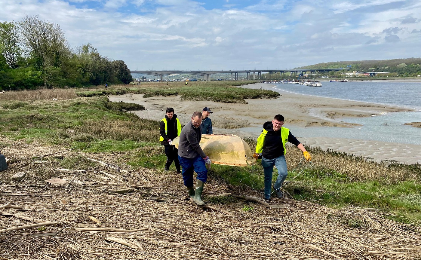 Volunteers carry a fibreglass dinghy, rather the worse for wear, up from the foreshore