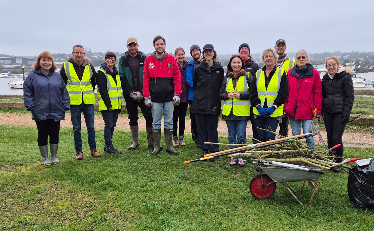 A group of volunteers in front of the sea wall in Esplanade Gardens, with a barrow full of chopped branches and a bag full of garden waste