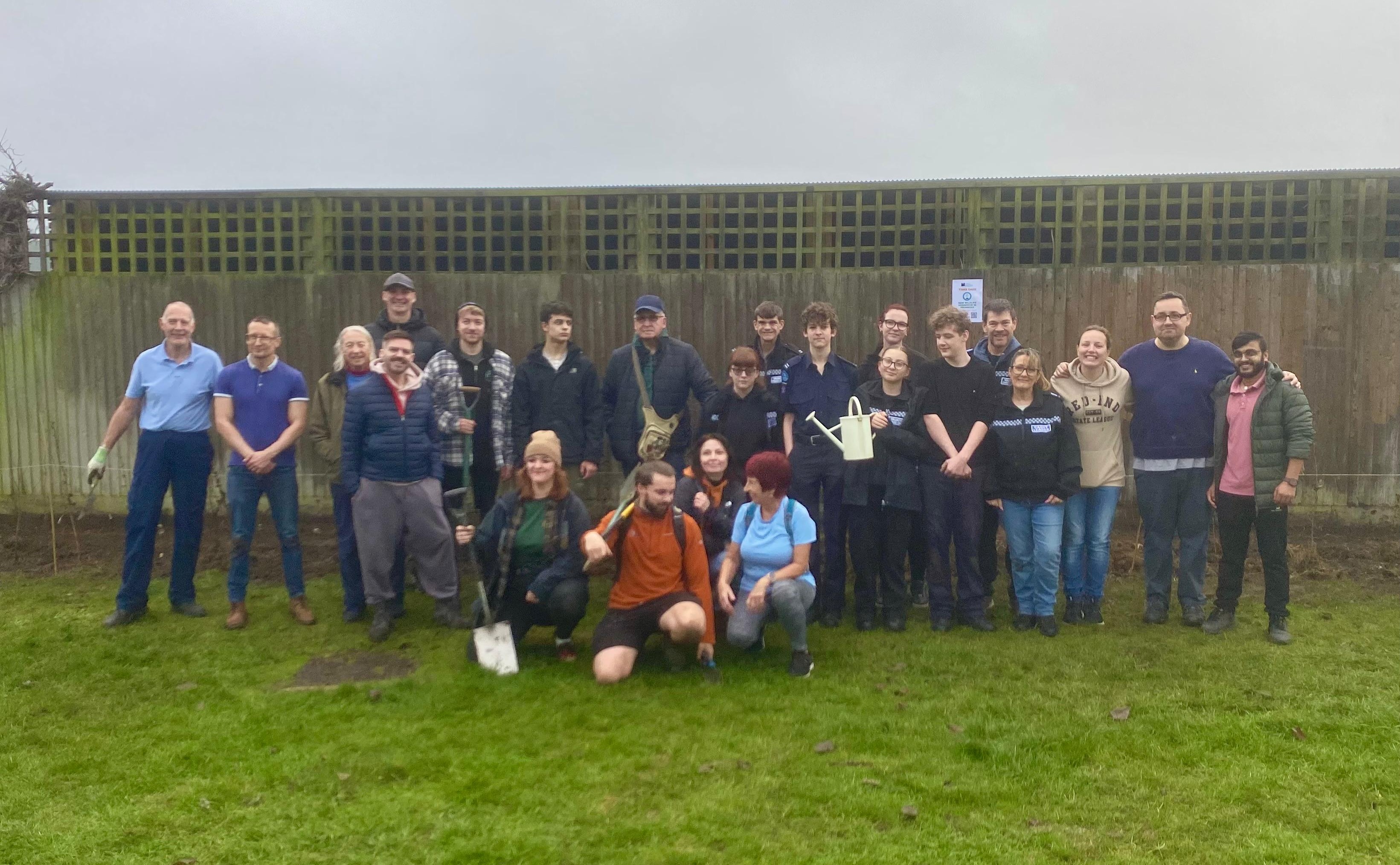A group photo of the twenty or so volunteers that attended this activity, standing in front of the newly planted whips and the Hathaway Court fence