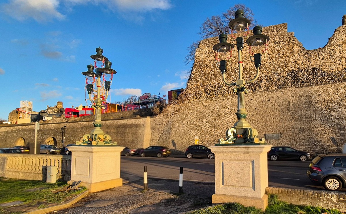 Ornate Edwardian lights in classic style atop granite plinths at the entrance to Esplanade Gardens with the walls of Rochester Castle behind